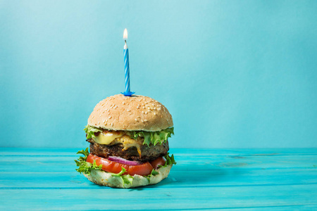 自制汉堡烧烤三明治与牛肉和点燃蜡烛在蓝色背景生日聚会.