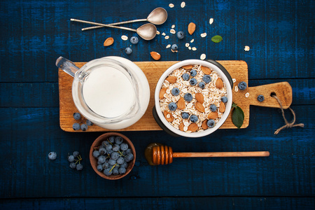 蓝底白字黑木制健康的早餐 燕麦粥 牛奶 蓝莓 蜂蜜和杏仁。乡村风格