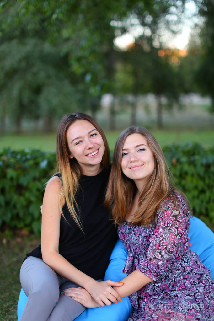 两个迷人的女孩坐在椅子上,旁边彼此微笑