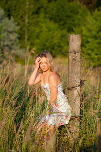 美丽的年轻女子站在田野附近的一个混凝土柱, 绿色的草和花朵。户外享受大自然。健康微笑的女孩站在高高的草丛中