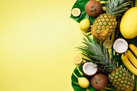 异国情调的菠萝, 成熟的椰子, 香蕉, 瓜, 柠檬, 热带棕榈和绿色的龟背竹叶子在黄色背景与 copyspace。创意布局。单色