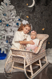 两个可爱的真正的孩子姐妹在黑色背景上摆出一棵白色的圣诞树在一起