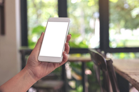 图像的一个女人拿着看着一个白色的智能手机与空白桌面屏幕与模糊绿色自然背景