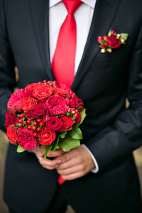 新郎控股新娘花束关闭。花园里的红玫瑰装饰的组成