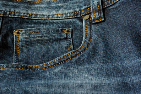 一条蓝色牛仔裤的特写, 上面有橙色的缝线。口袋与铆钉特写