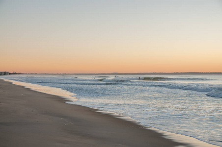 在大西洋沿岸的一个温和的清晨。冲浪者骑在远处的波浪上。美国。缅因州