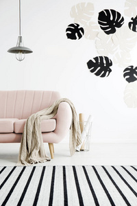 毯子在粉红色的沙发下, 在客厅内的灯, 带条纹地毯和树叶。真实照片