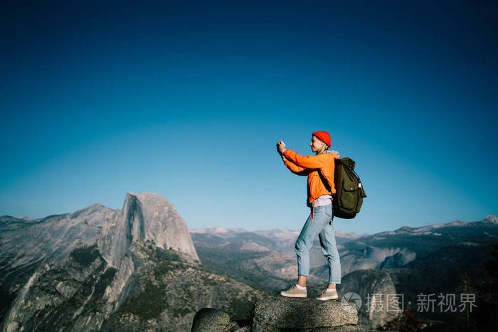 女性旅行者与背包拍照的智能手机站在山顶上惊险的景观视图, 女孩做