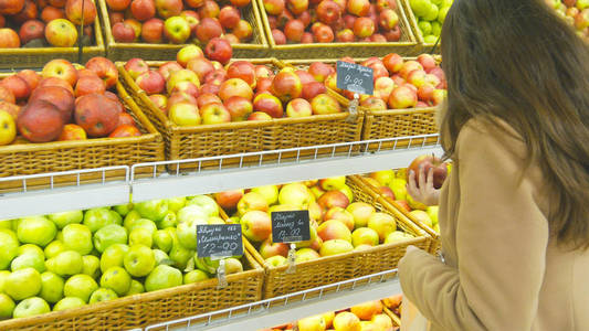 女人在杂货店中选择新鲜的红苹果生产部并将它放在塑料袋里。年轻漂亮的女孩超市并将它们放入购物篮中选择苹果。关闭