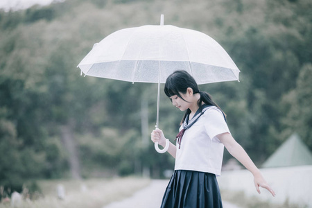 在雨中漫步在自然人行道上的亚洲学校女孩肖像