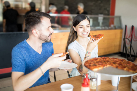 有魅力的女人和英俊的男人享受香肠比萨饼在比萨店午餐期间, 同时举行比萨饼切片和交谈