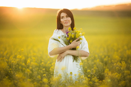 快乐的年轻妇女与花束野花在黄色领域, 日落时间