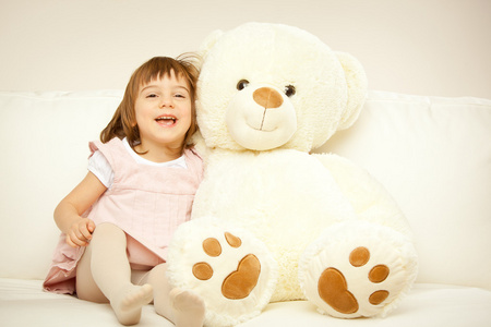 金发碧眼的女孩子和她白色的玩具熊在床上玩