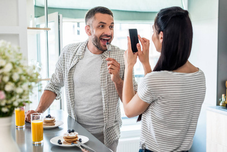妇女拍照的丈夫玩早餐在柜台在厨房