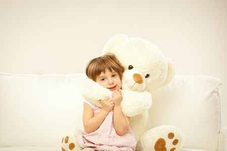 金发碧眼的女孩子和她白色的玩具熊在床上玩