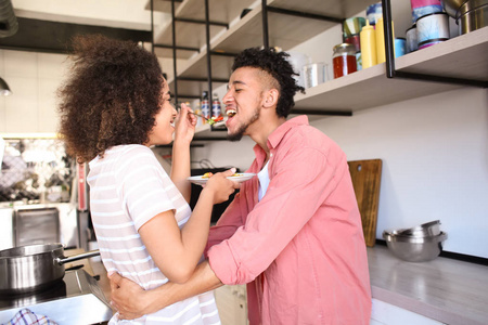 年轻的非洲裔美国人情侣拥抱和品尝厨房的食物