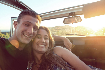 愉快的年轻夫妇在汽车享受美丽的日落在乡下