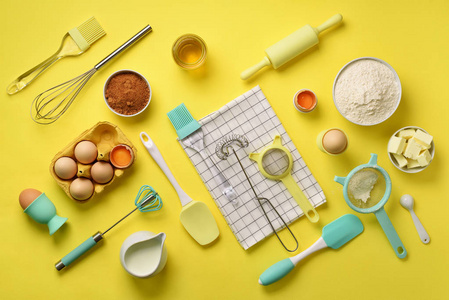 健康烘焙配料黄油, 糖, 面粉, 鸡蛋, 油, 勺子, 滚针, 刷子, 扫, 毛巾在黄色背景。烘焙食品框架, 烹饪理念。顶部视