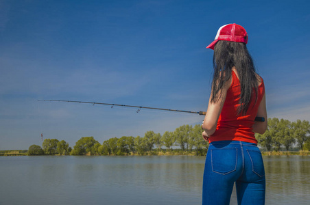 在湖边钓鱼的女人。后退视图