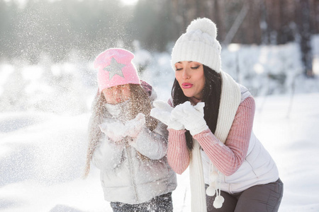 年轻漂亮的母亲和她的小女孩在户外在冬天的乐趣。开朗的孩子和她美丽的妈妈玩雪的性质。吹雪