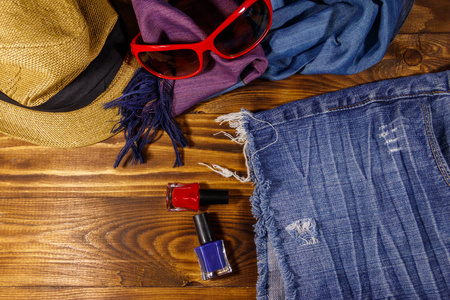 红色太阳镜, 草帽, 夏季围巾, 牛仔裤短裤和指甲油在木质背景。女装时尚饰品。暑假和旅行概念