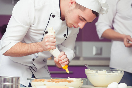 提拉米苏烹饪, 及格考试的概念。在厨师制服的认真集中的实习生的画像做意大利甜点在现代厨房。室内拍摄
