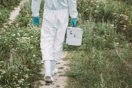 男性科学家在草地上的工作手提箱行走防护服的裁剪图像