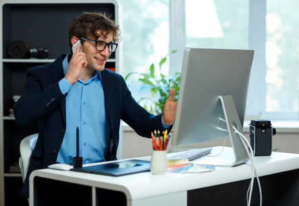 英俊的年轻男子从家庭办公室工作和使用智能手机照片