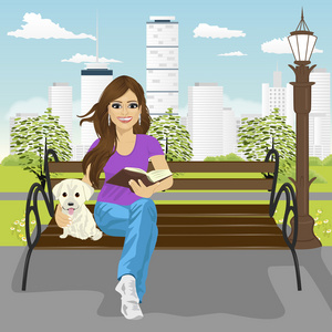 年轻幸福的女人享受空闲时间在城市公园在夏天阅读本书坐在长椅上拥抱拉布拉多小狗