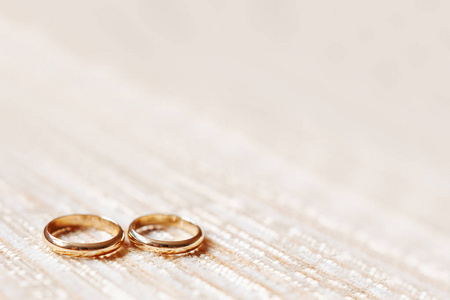 金色婚礼戒指上米色面料的背景。婚礼的细节, 象征爱情和婚姻。文本位置
