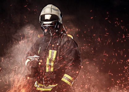 一名职业消防员身着制服和氧气面罩站在火灾火花和烟雾在黑暗的背景下