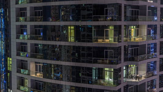 晚上 timelapse 的摩天大楼的窗户。现代住宅高层建筑在迪拜码头的看法。人们在公寓里搬家。空中俯视图。放大