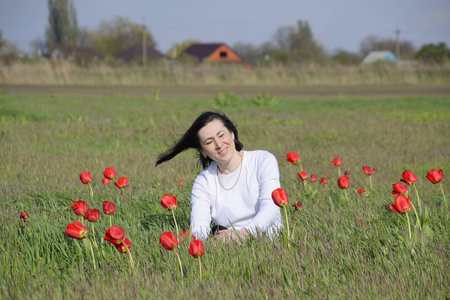 美丽的仙女少女在田野中花丛中盛开。一个女孩在红色的花朵和绿色的田野背景的肖像。郁金香领域