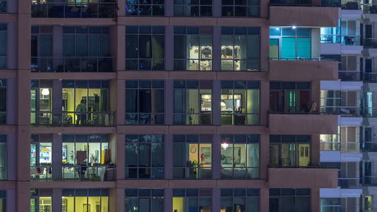 晚上 timelapse 的摩天大楼的窗户。现代住宅和办公室高层建筑的看法在迪拜码头。人们搬到里面去。空中俯视图。缩小