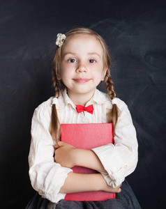 孩子女孩在学校制服衣裳与书在粉笔板背景 孩子56 岁。回到学校小学和教育理念