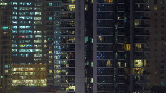 在夜晚 timelapse 的摩天大楼上闪闪发光的窗户。现代住宅和办公室高层建筑的看法在迪拜码头。人们搬到里面去。空中俯视图。平
