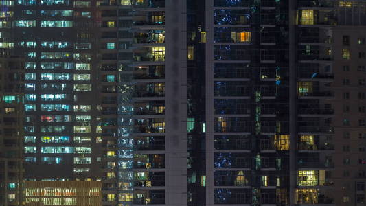 在夜晚 timelapse 的摩天大楼上闪闪发光的窗户。现代住宅和办公室高层建筑的看法在迪拜码头。人们搬到里面去。空中俯视图。放