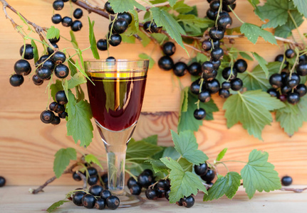 醋栗利口酒自制的甜酒由黑醋栗和新鲜浆果在树枝上, 老式木质背景照片