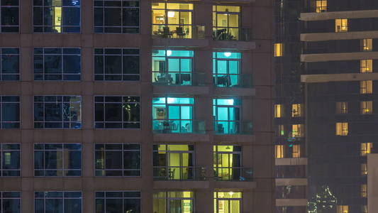窗户的多层建筑玻璃和钢照明内和移动的人在 timelapse。现代住宅摩天大楼在迪拜码头的鸟瞰图。向下平移