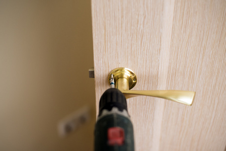 安装门锁使用到螺丝刀。木匠在锁安装时用电动钻进木头门