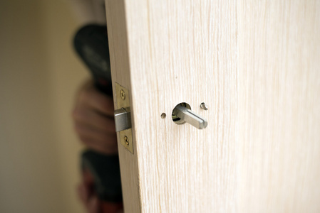安装门锁使用到螺丝刀。木匠在锁安装时用电动钻进木头门