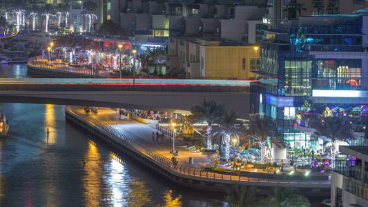 水运河和海滨长廊在迪拜码头的天际线在晚上 timelapse。带有照明和照明的住宅大楼。在摩天大楼附近的一座桥上漂浮着的游艇和小