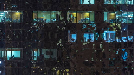 窗户的多层建筑玻璃和钢照明内和移动的人在 timelapse。在迪拜, 现代办公摩天大楼的鸟瞰图。缩小