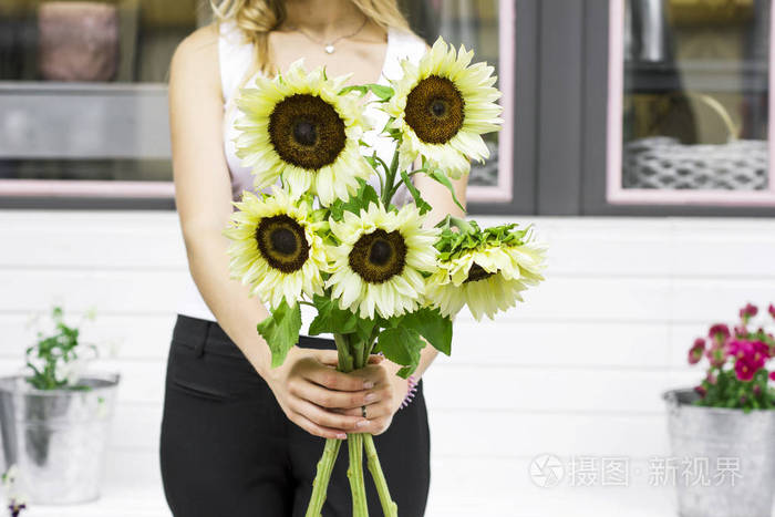 年轻女子手持装饰性淡黄色向日葵在街道附近花店