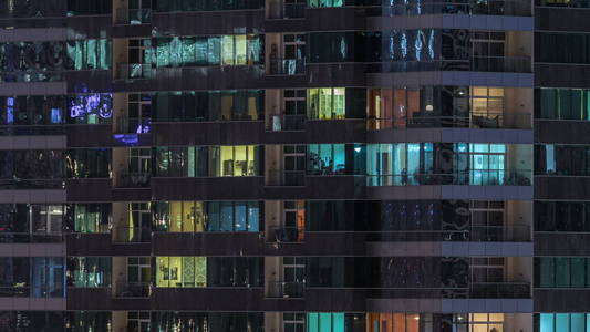 窗户的多层建筑玻璃和钢照明内和移动的人在 timelapse。迪拜现代住宅摩天大楼鸟瞰图