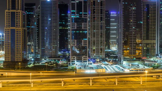 在整个夜晚, timelapse 在酋长扎耶德路和地铁线上的交通, 有照明摩天大楼的朱美拉湖塔的鸟瞰图。从迪拜码头的屋顶景观