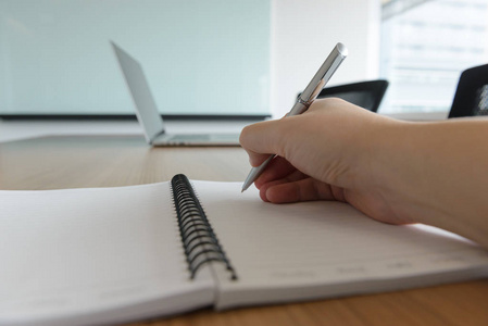 人用右手边的钢笔在办公室或会议室的笔记本上