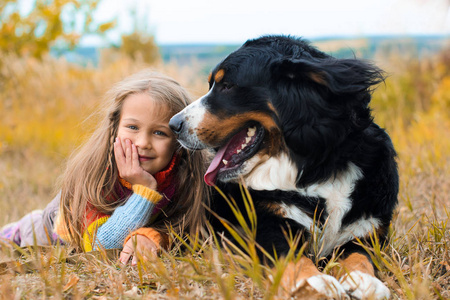 女孩与狗 Berner Sennenhund 躺在秋天的草地上