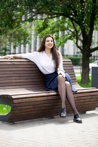 年轻美丽的黑发女人坐在夏天公园的长椅上