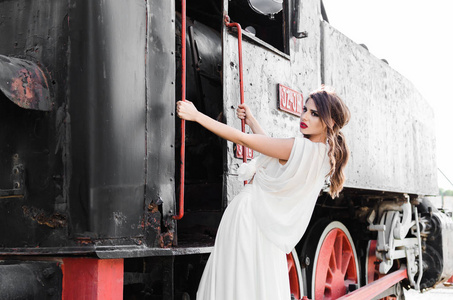 漂亮的年轻女子坐在铁路旁边的旧火车穿着长白色的礼服